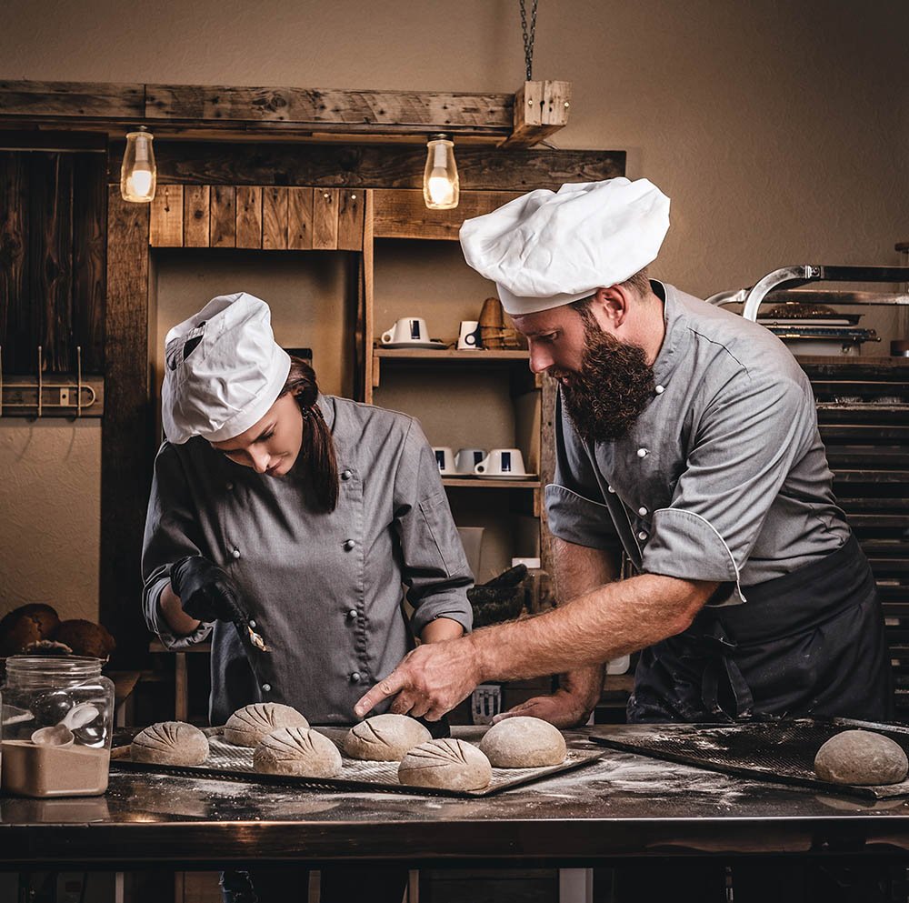 Chef teaching his assistant to bake the bread in a bakery.
